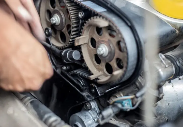 Meccanico lavora sul motore, sostituendo la cinghia di distribuzione. Il costo di questa operazione è importante per la manutenzione.