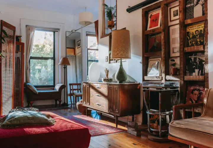 A cozy living room with vintage wood furniture styles, featuring a mid-century dresser, a wooden shelf unit displaying records, and a comfortable armchair.