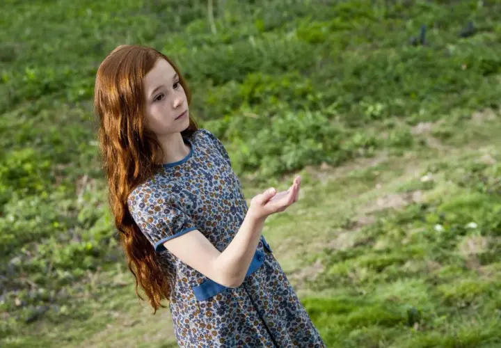 Ruda dziewczynka w kwiecistej sukience, Lily Potter, wyciąga dłoń w stronę zielonej łąki.