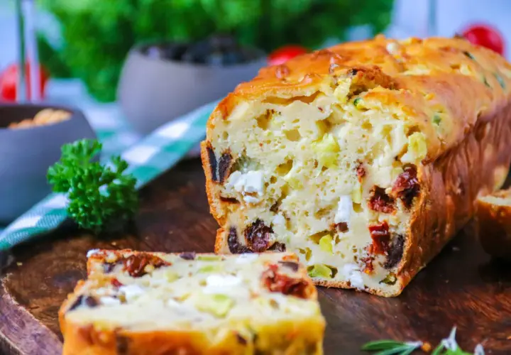 Un délicieux cake salé aux olives, tomates séchées et feta, coupé en tranches sur une planche en bois.