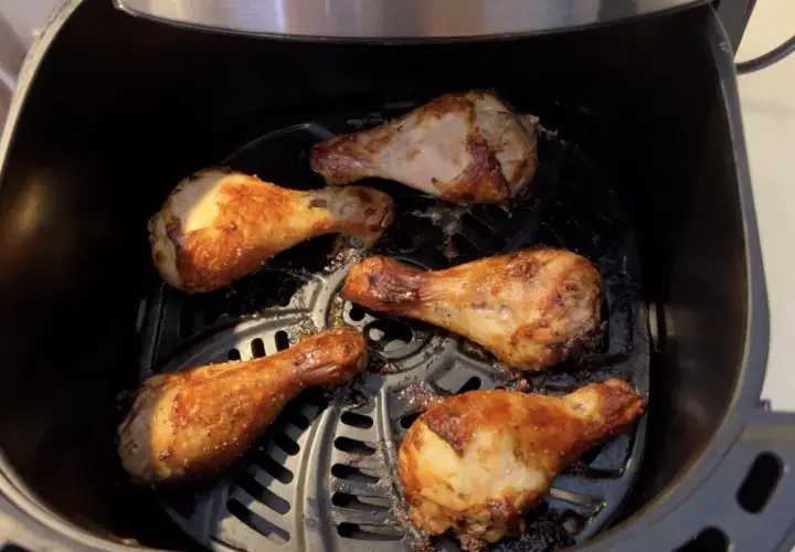 Cinq pilons de poulet dorés et croustillants cuisent dans une friteuse à air.