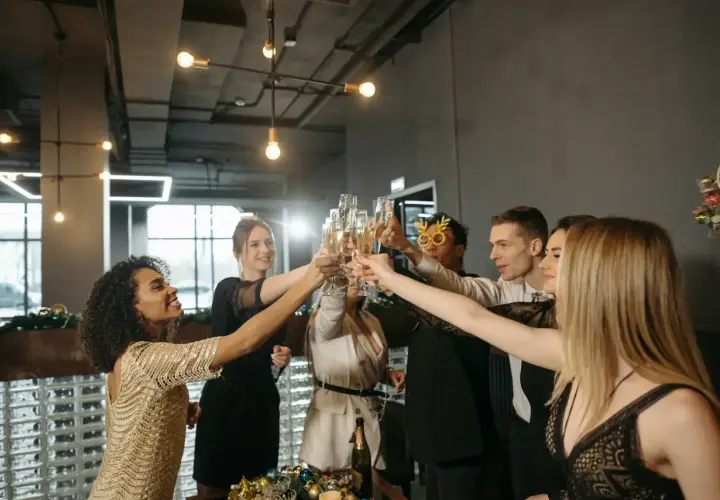 Grupa ludzi w eleganckich strojach na uroczystą kolację firmową wznosi toasty szampanem.