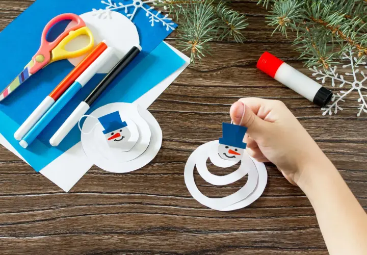 Niño crea muñecos de nieve con manualidades de invierno. Tijeras, rotuladores y pegamento listos para la diversión.