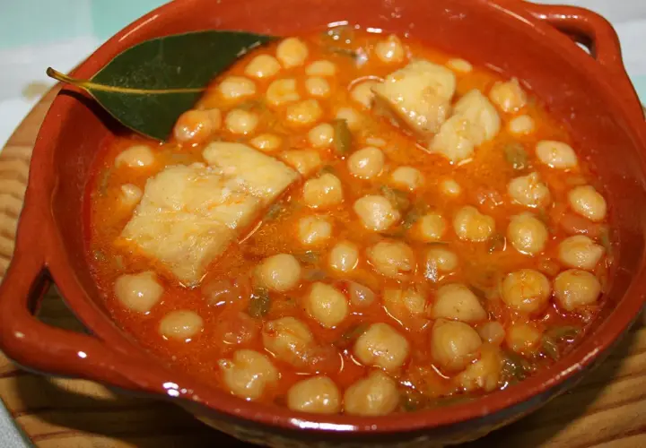 Garbanzos con bacalao, la receta de la abuela, servidos en cazuela de barro con hoja de laurel.