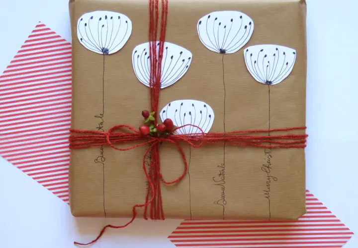Confezioni pacchi regalo creativi con fiori stilizzati e bacche rosse, legati con spago rosso. Scritte "Buon Natale" e "Merry Christmas".