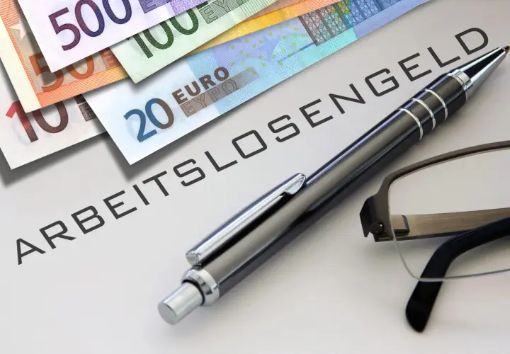 Euro-Scheine liegen neben einem Stift und einer Brille auf einem Dokument mit der Aufschrift "ABFINDUNG ARBEITSLOSENGELD".