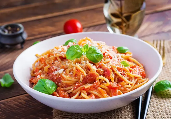 Un piatto di spaghetti alla corte d'assise, conditi con pomodoro fresco e basilico, spolverati di parmigiano.