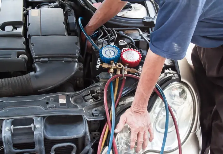 Mecánico realizando la tarea de cargar gas aire acondicionado en un coche, con manómetros y mangueras conectadas al motor.