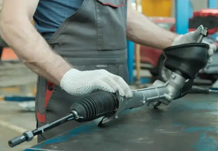 Mechanik w białych rękawiczkach trzyma element układu kierowniczego samochodu.