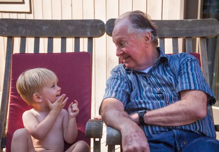 Un abuelo sonríe a su nieto, un momento tierno que los padres disfrutan al dejar a sus hijos con los abuelos.