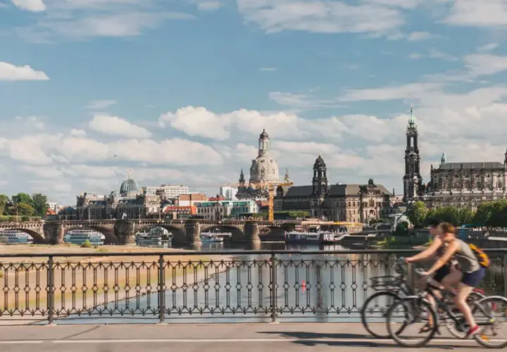 Two people enjoy bike tours in Germany, cycling across a bridge with a scenic view of Dresden's historic skyline.