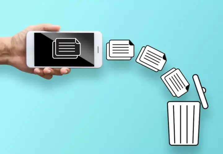 Dłoń trzyma smartfon, z którego ikony dokumentów lecą do kosza. Dowiedz się, jak przywrócić usunięte pliki z kosza.