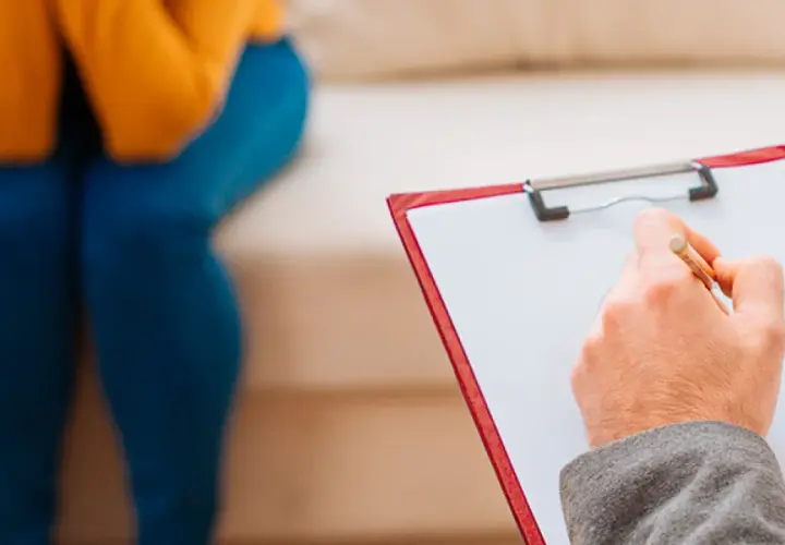 Seduta in terapia, con un professionista che prende appunti. Un passo verso il benessere, forse un giorno con assicurazione psicologi obbligatoria.
