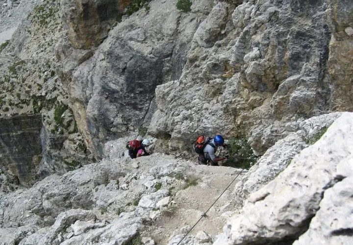 Dwóch wspinaczy pokonuje trudną trasę na ferratach w Dolomitach, korzystając z liny asekuracyjnej.