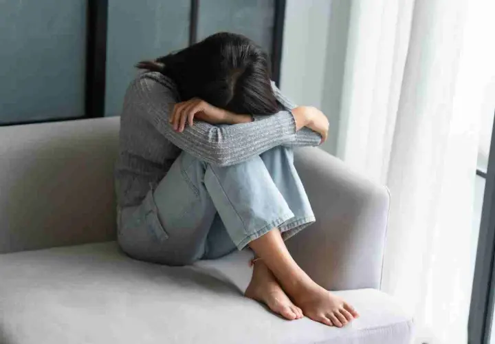 Ragazza rannicchiata sul divano, con la testa tra le ginocchia, soffre di fobia del vomito.