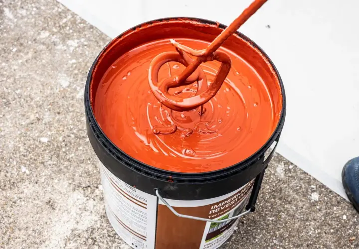 Mezclando pintura impermeabilizante naranja en un cubo. El tiempo secado pintura impermeabilizante es clave para un buen acabado.