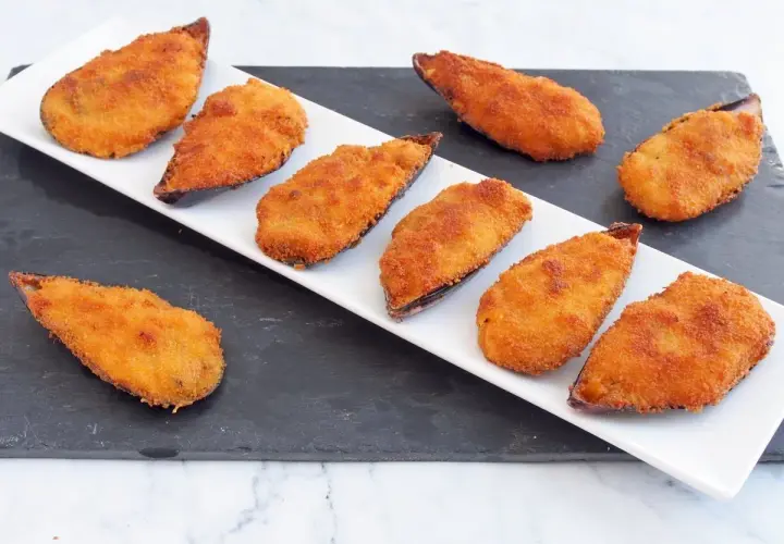 Ocho mejillones tigre dorados y crujientes, servidos en una bandeja blanca sobre una pizarra.