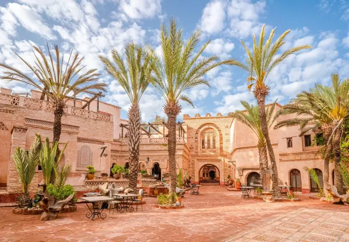 Sonniger Innenhof in der Agadir Altstadt mit Palmen, traditioneller Architektur und Sitzgelegenheiten im Freien.