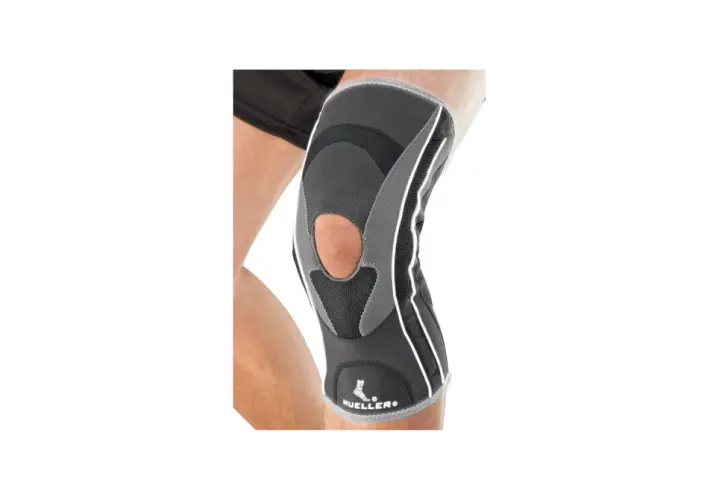Szary stabilizator kolana Mueller HG80 z otworem na rzepkę, na nodze.