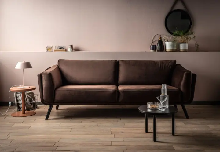 Elegancka kanapa w odcieniu barwy brązowej, obok stolik z lampką i dekoracjami.