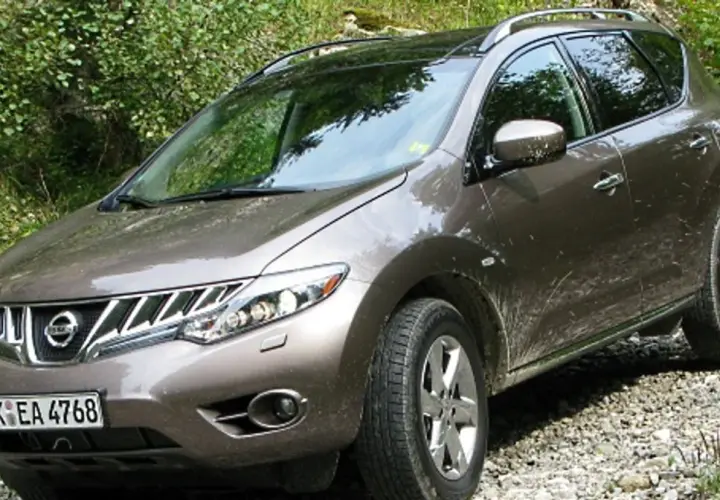 Brązowy Nissan Murano na kamienistej drodze, otoczony zielenią.