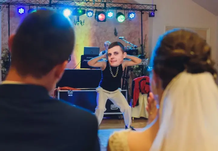 Zabawny moment podczas oczepin weselnych. Pan młody tańczy z wielką głową na szyi, a para młoda obserwuje go z uśmiechem.