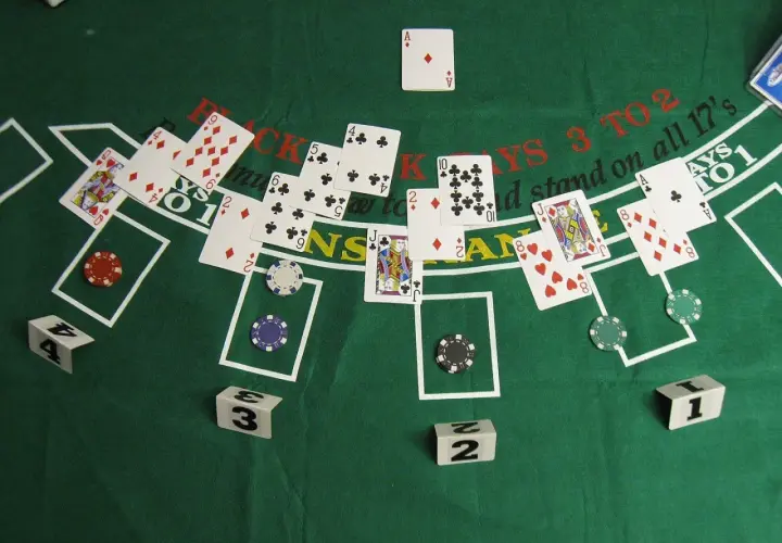 Kier karty na zielonym stole do blackjacka. Widoczne karty, żetony i kostki z numerami.