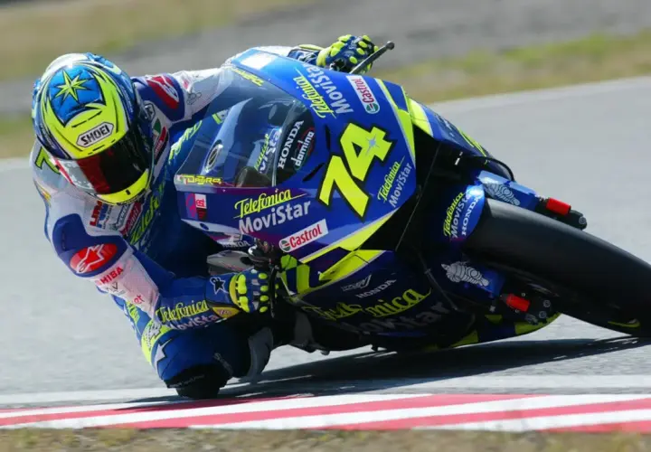 Daijiro Kato inclinado en su moto azul y amarilla, número 74, en una curva cerrada.