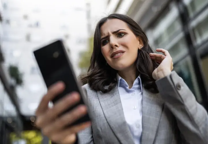 Zmartwiona kobieta próbuje odzyskać hasło do FB, patrząc na telefon.
