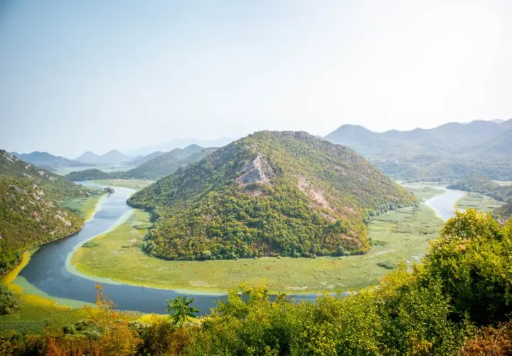 A winding river snakes through lush green hills and a vast wetland, a perfect scene for planning how many days in Montenegro.