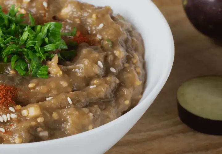 En krämig baba ganoush toppad med färsk persilja och paprikapulver. Bredvid syns skivade auberginer.