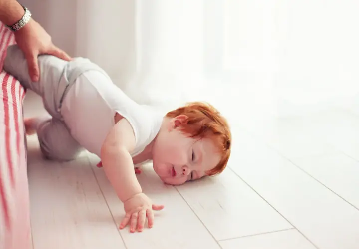 Un bimbo con capelli rossi è caduto dal letto. Un adulto lo tiene per la gamba. Non c'è motivo di preoccuparsi, è solo un piccolo capitombolo.