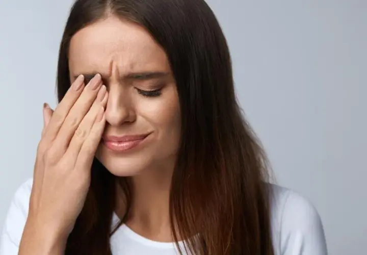 Kobieta zamyka oczy, pocierając je dłonią. Może to być jeden z objawów zespołu Sjogrena, który powoduje suchość oczu.