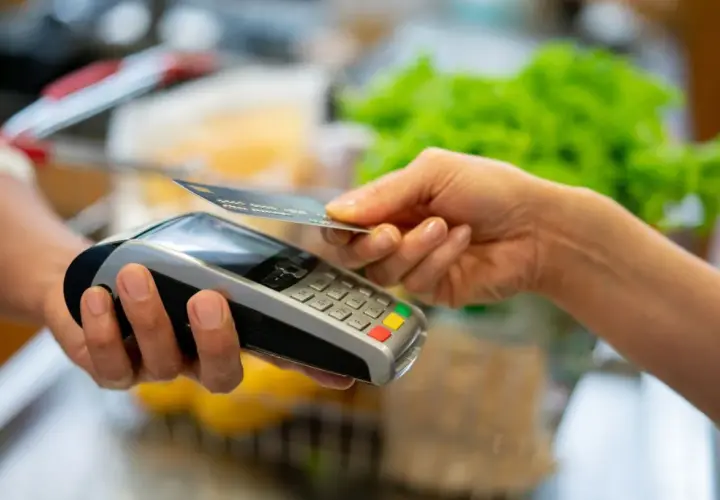 Une main approche une carte bancaire d'un terminal de paiement pour un paiement sans contact.
