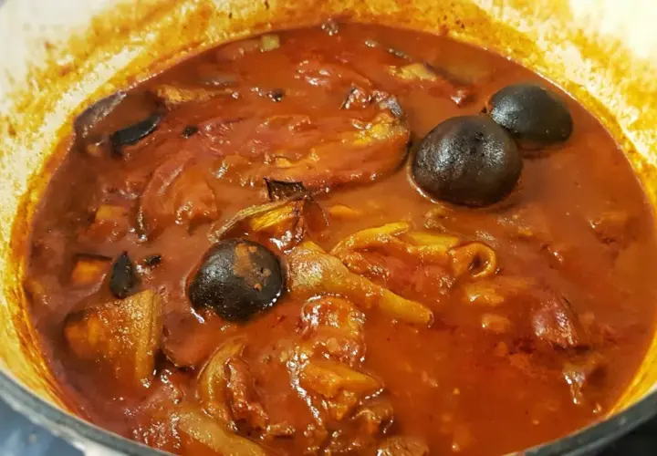 Khoresh Bademjan, a Persian eggplant stew, simmering in a pot with whole dried limes and chunks of eggplant.