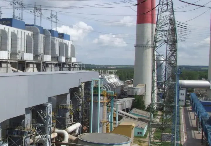 Duże budynki elektrowni z niebieskimi elementami, wysokie kominy z czerwonymi pasami i linie energetyczne.