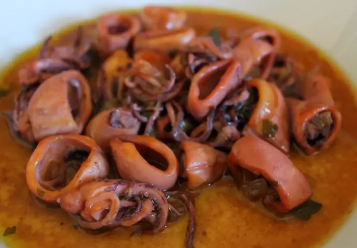 Calamares en salsa, tiernos y jugosos, con sus tentáculos enrollados, nadan en un rico caldo dorado.