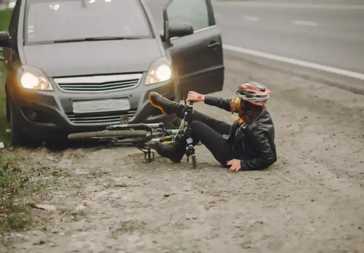 Kobieta w kasku leży obok przewróconego roweru, obok stoi samochód z otwartymi drzwiami. Wygląda na to, że doszło do ucieczki z miejsca kolizji.
