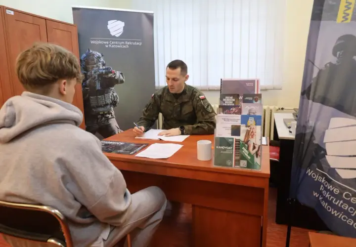 Młody mężczyzna siedzi przed żołnierzem, który wypełnia dokumenty. To rozmowa kwalifikacyjna w Wojskowym Centrum Rekrutacji.