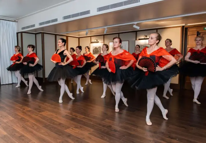 Un gruppo di ballerine con tutù neri e scialli rossi, che tengono ventagli, dimostra cos'è la danza classica con grazia ed eleganza.