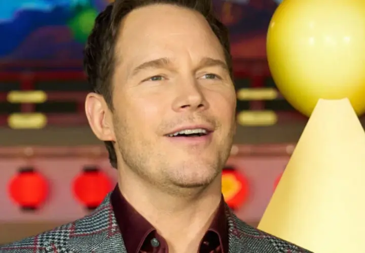 Chris Pratt, gwiazda wielu filmów, uśmiecha się na tle czerwonych lampionów i żółtej dekoracji.