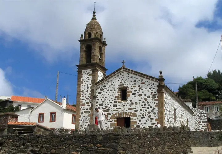 Iglesia de San Andrés de Teixido, con su campanario y fachada de piedra y cal, bajo un cielo nublado.