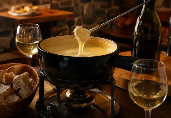 Un réchaud chauffe une fondue savoyarde crémeuse, accompagnée de pain et d'un verre de vin pour fondue savoyarde.