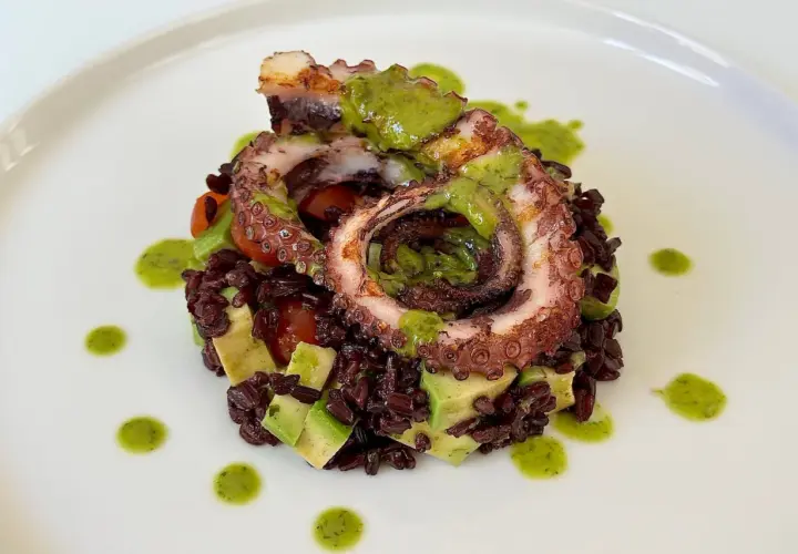 Delizioso polpo alla griglia servito su riso venere con avocado e pomodorini, condito con salsa verde.