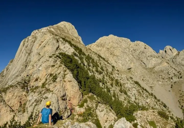 Un excursionista con casco amarillo contempla imponentes montañas, un paisaje ideal para rutas por Berga.