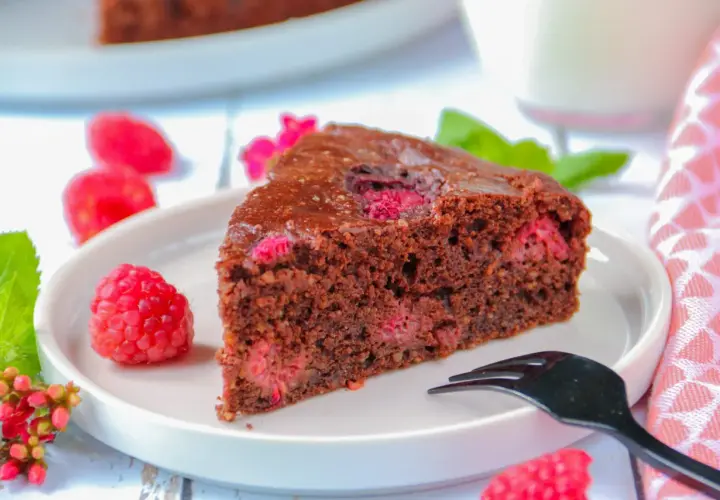 Tranche de gâteau au chocolat et framboise sans gluten, décorée de fruits frais et d'une touche de menthe.