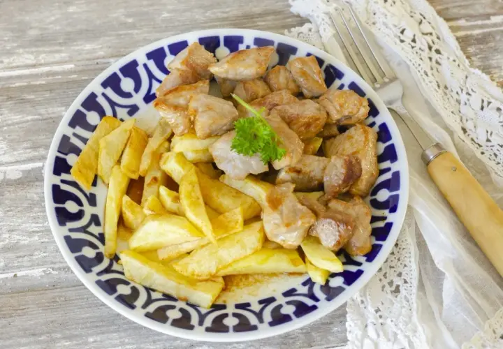 Un plato de raxo con patatas fritas, decorado con perejil fresco. Un clásico delicioso.