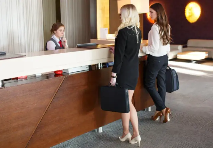 La receptionist accoglie i clienti che arrivano in albergo. Due donne d'affari con valigette attendono al bancone.