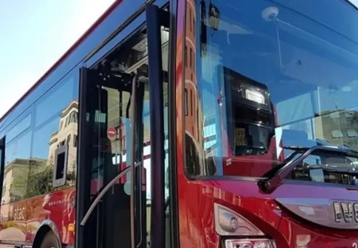 Autobus rosso con porte aperte, riflessi di palazzi sui vetri. Forse l'ultima metro della giornata, ma è un bus.