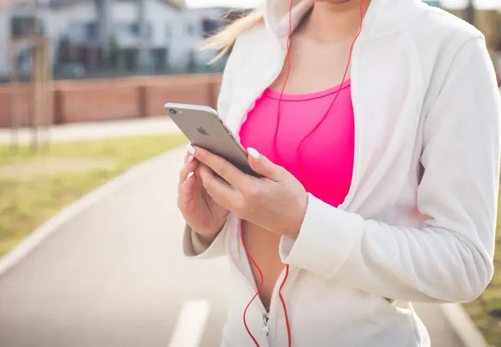 Kobieta w sportowym stroju trzyma iPhone'a, słuchając muzyki. Chcesz wiedzieć, jak włączyć Siri?